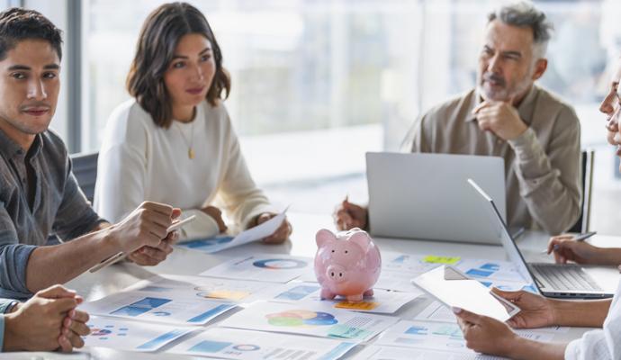 Group of business people in a meeting reviewing financial documents with a piggy bank sitting on top