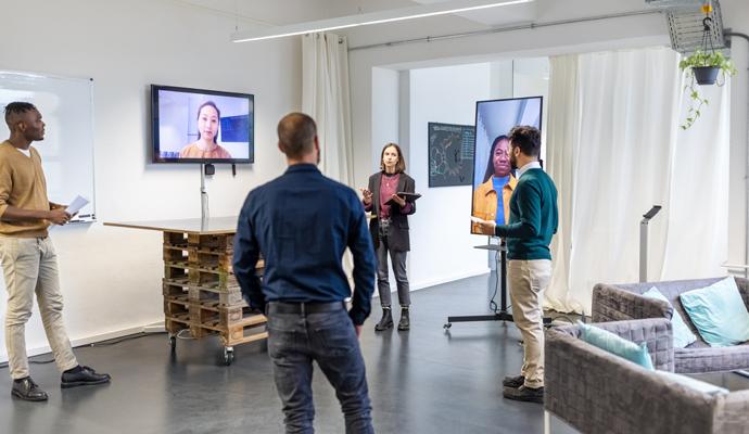 Business people standing and discussing with colleagues joining meeting via video call.