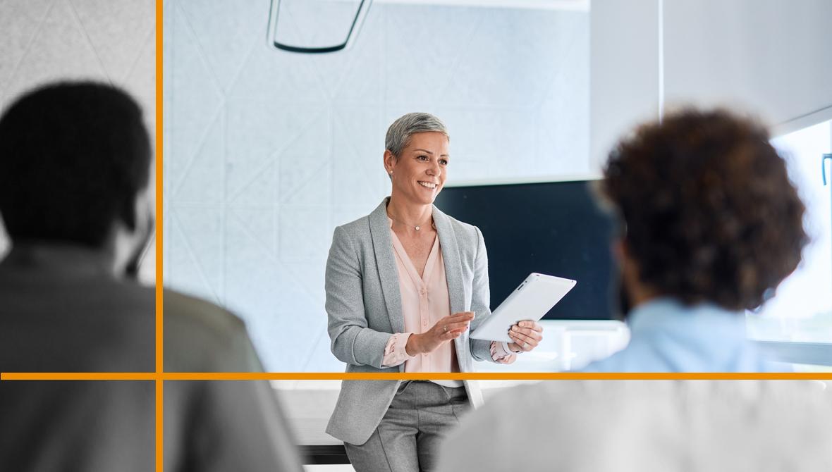A businesswoman holds a digital tablet while leading a small group meeting