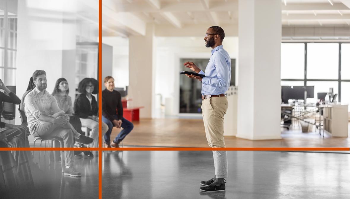 : A businessman stands and addresses his seated colleagues with a digital tablet in hand.