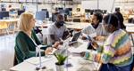 Five colleagues sit at a table in a casual open-office environment for a planning session.