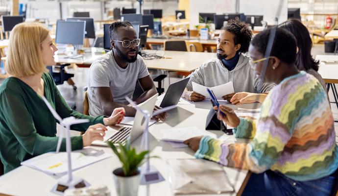 Five colleagues sit at a table in a casual open-office environment for a planning session.