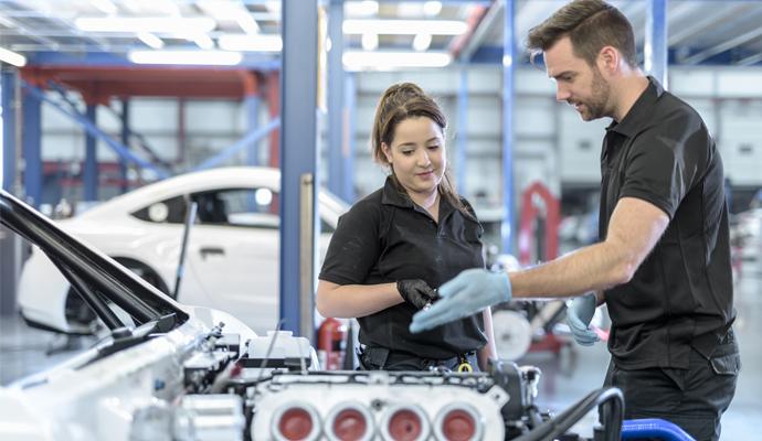 Two engineers look at and discuss the engine of a car in a factory