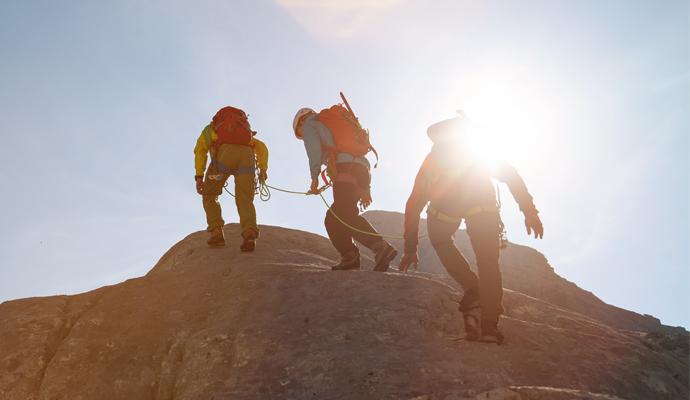 Photo of three mountain climbers, connected by a rope, approaching a summit
