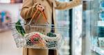 Cropped photo of a woman carrying a shopping basket and reaching into a refrigerated case in a supermarket