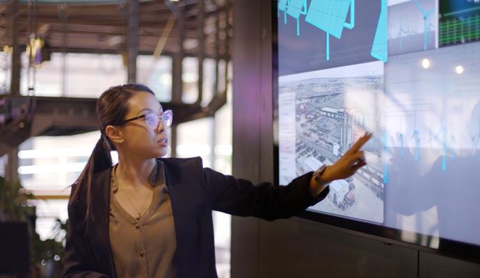 A woman presenting with a large touchscreen displaying technical diagrams and images