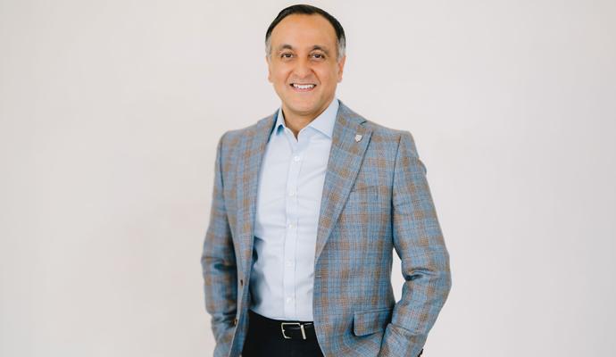 Zahid Salman, wearing a light blue dress shirt and a blue-gray plaid blazer, smiling against a plain background.