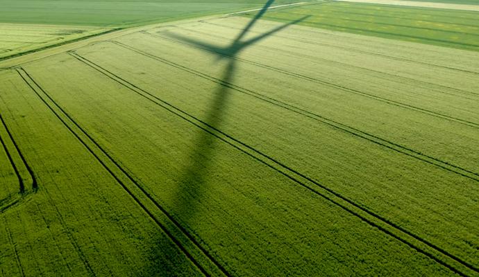 A wind turbine casts a long shadow across a green agricultural field.