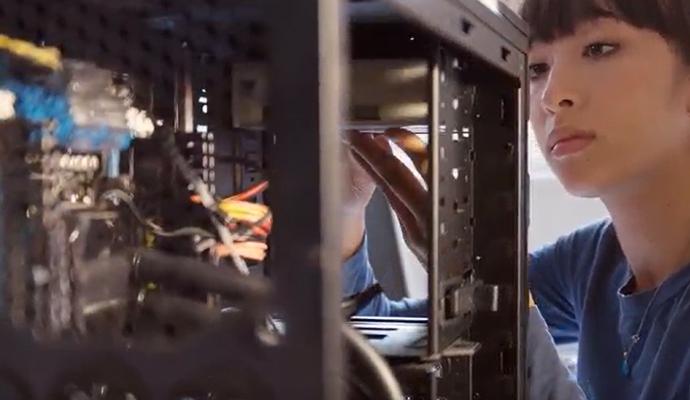 A woman works inside an open computer tower, adjusting components and wiring.