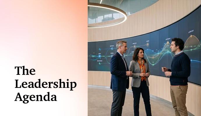 Three people meet in a modern building's lobby with a large digital display behind them.