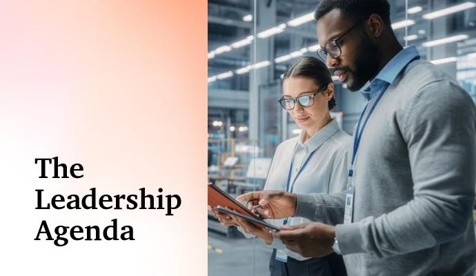 Two professionals standing in an industrial workspace, looking at a tablet together.