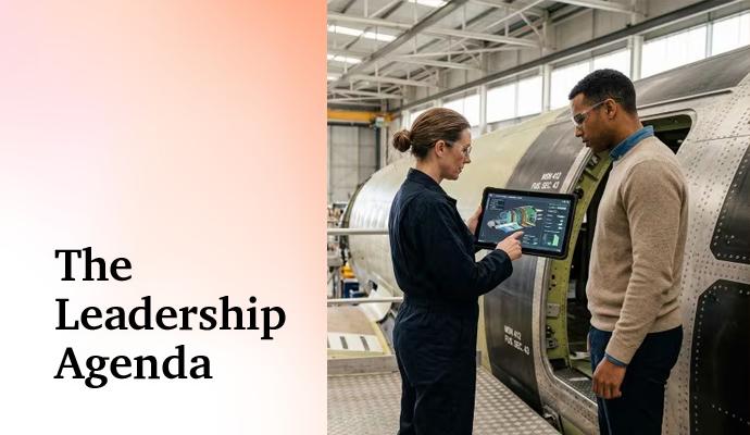Two professionals stand beside industrial equipment and review information on a digital tablet.
