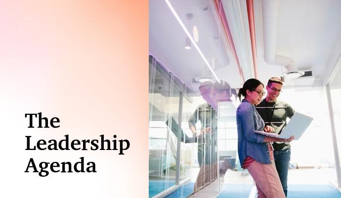 Coworkers collaborating on a project while standing in a bright, glass-walled workspace.