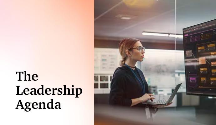 A woman holding a laptop and looking at a group of large monitors with the words “The Leadership Agenda” superimposed on the image