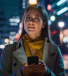 A woman standing in a city street at night holding a mobile device.